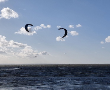 Dwa latawce kitesurfingowe nad wodą przy słonecznej pogodzie, pokazujące aktywną stronę zatoki.
